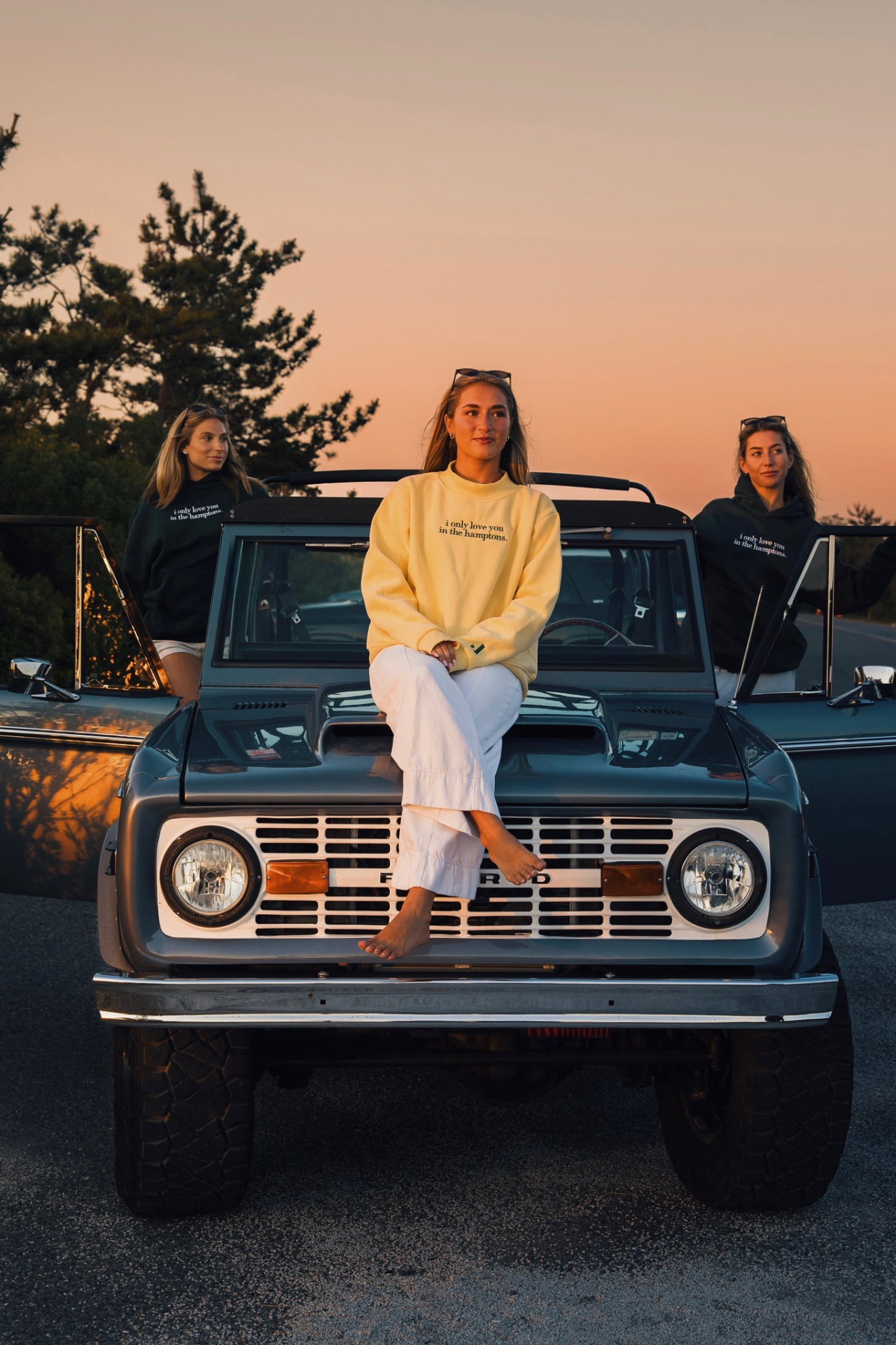 Three friends in i only love you in the hamptons hoodies at sunset on a vintage Bronco